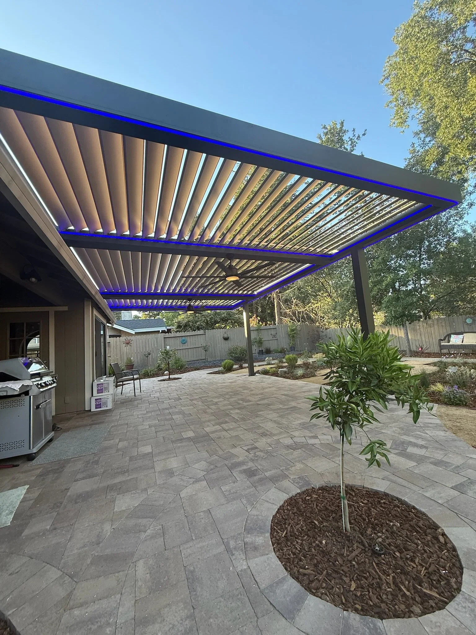 Aluminum louvered pergola with blue LED lighting over paver patio and outdoor kitchen