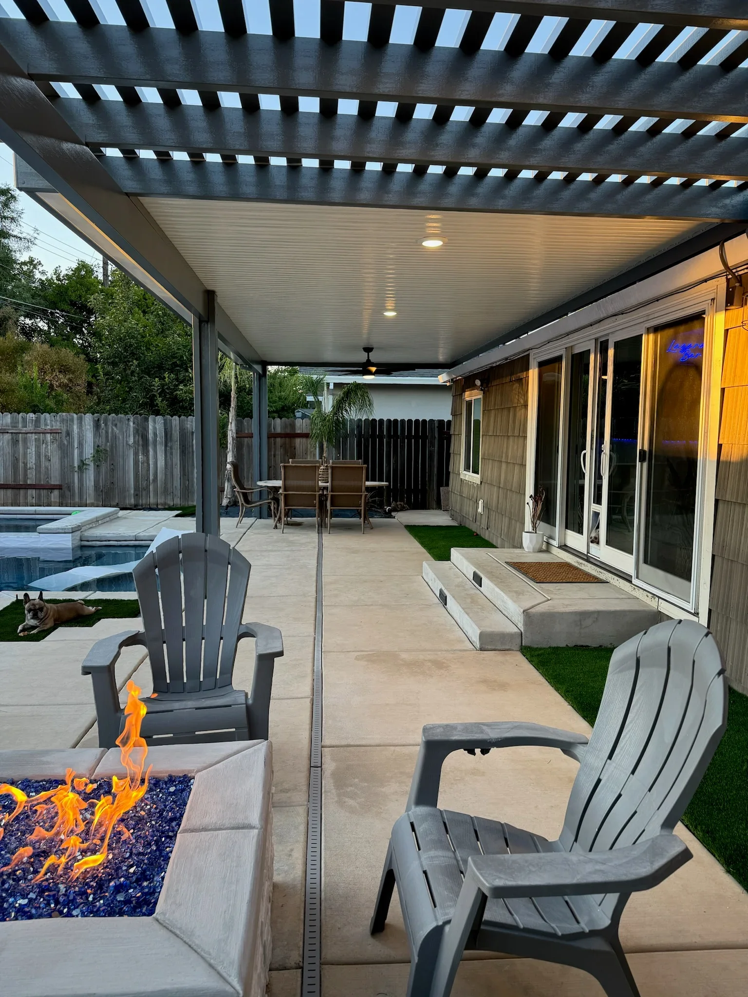 Black aluminum pergola with louver roof, recessed lighting, and concrete patio with fire pit