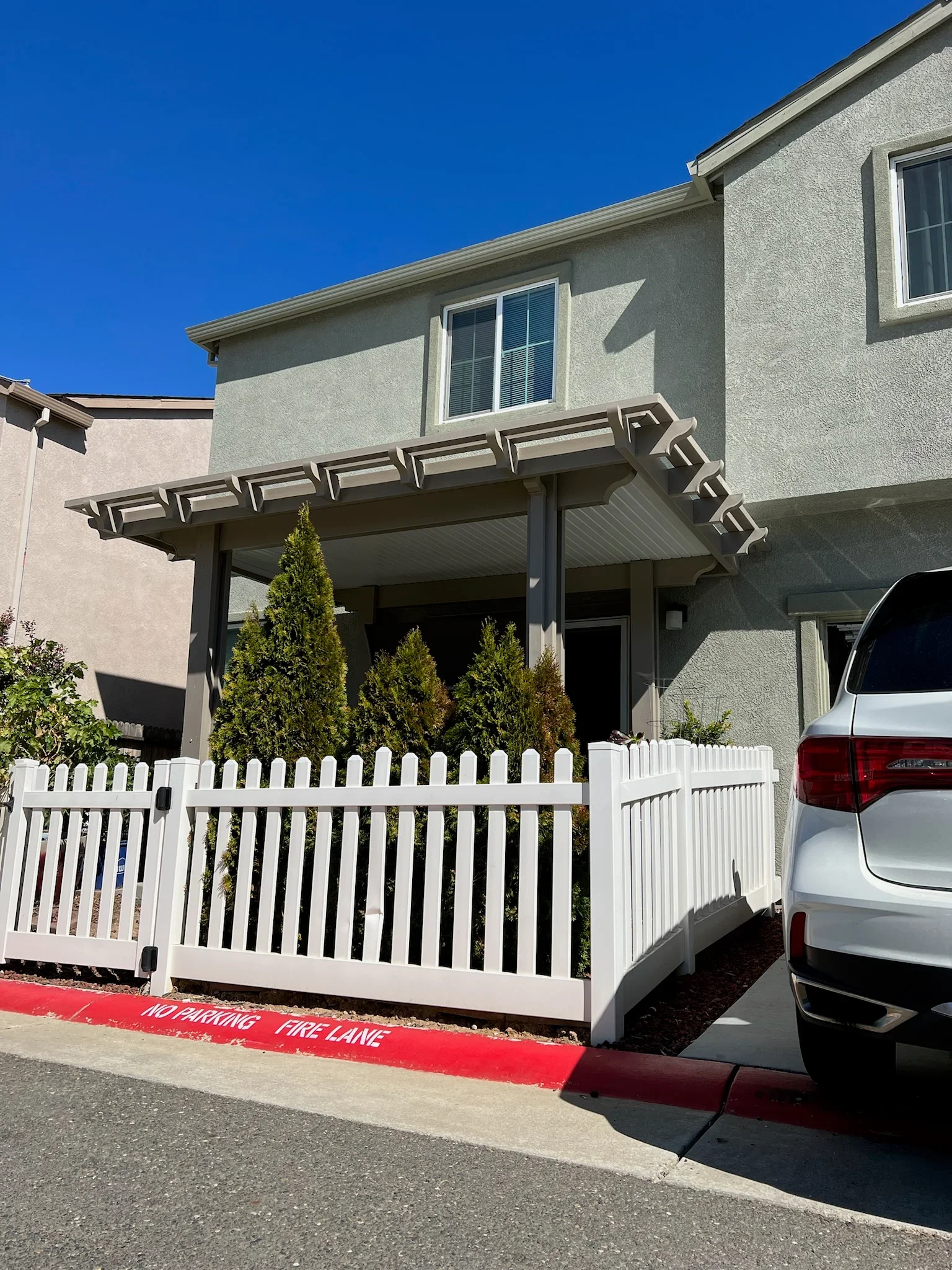 Modern pergola with geometric lattice overhead and white vinyl picket fencing at residential patio entrance