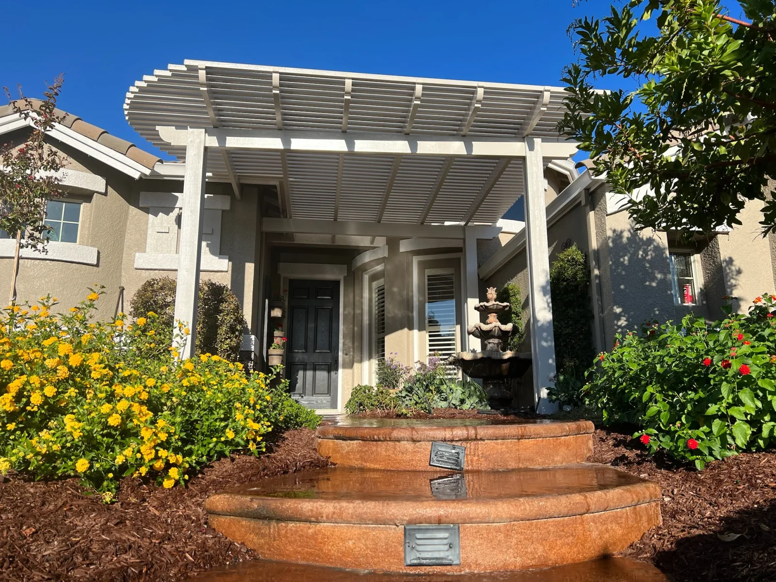 White aluminum pergola with louver slats over home entryway with landscaping