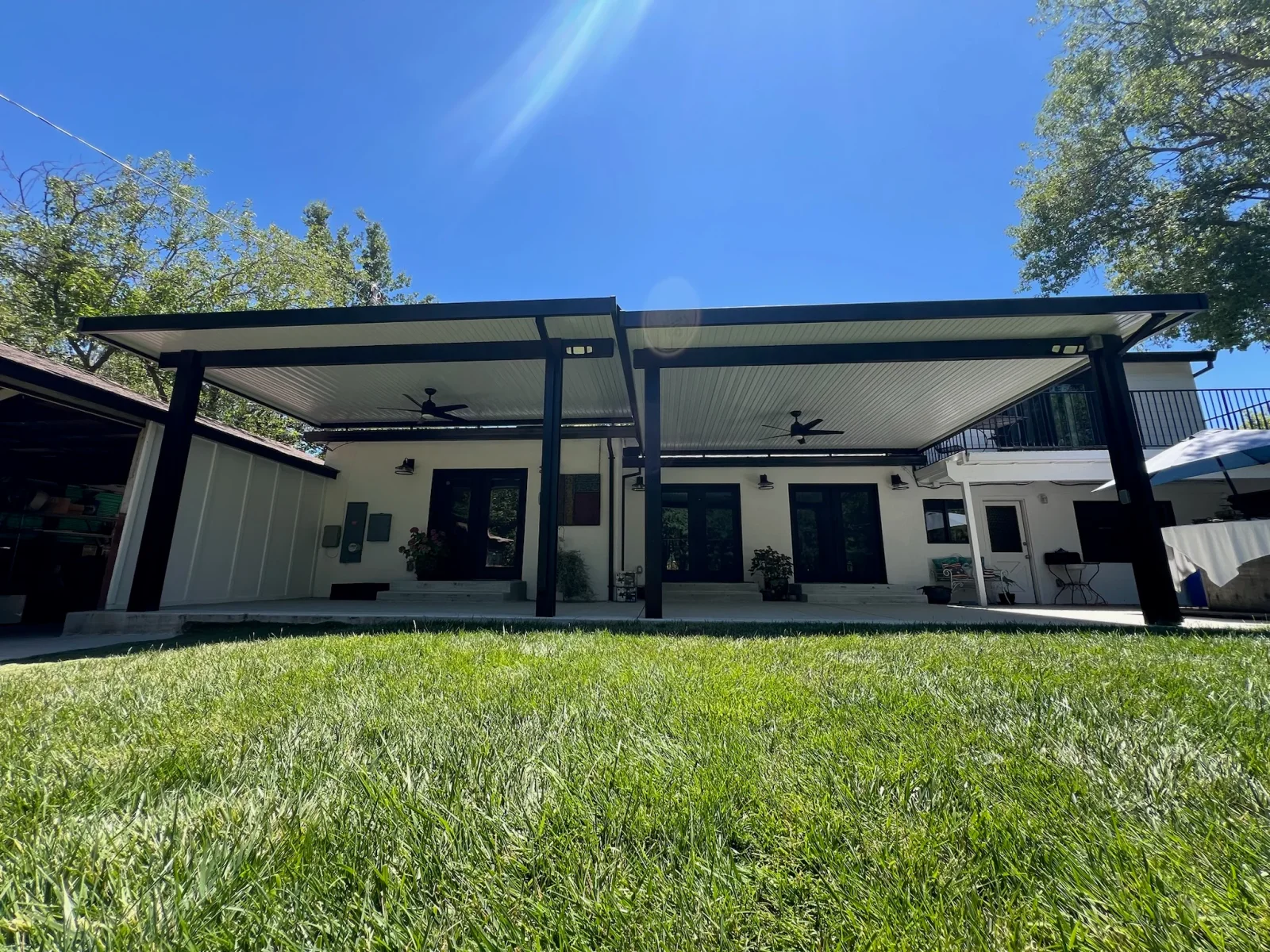 Black steel pergola with white metal ceiling panels and ceiling fans over concrete patio