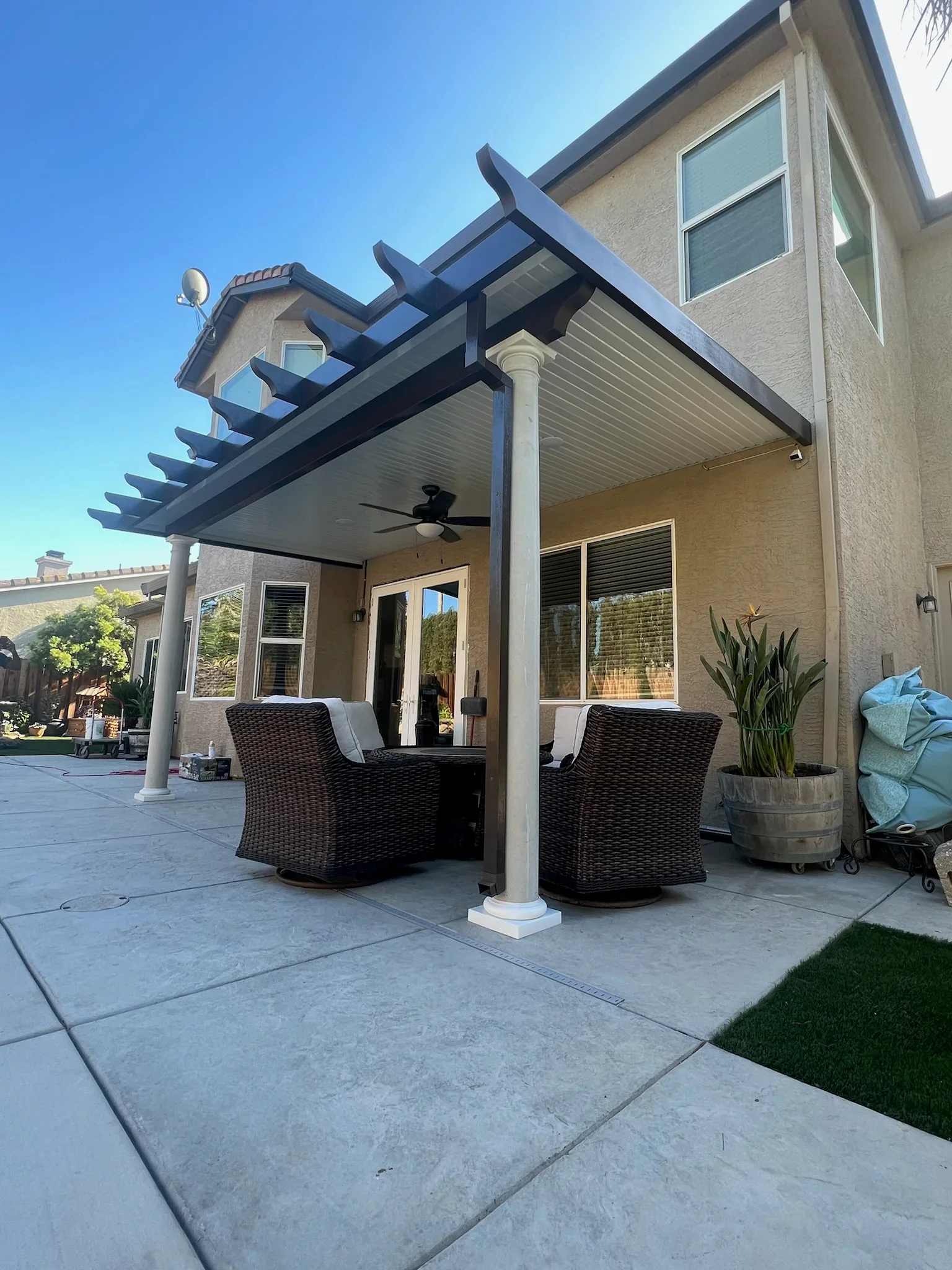 Louvered pergola with white column, motorized roof slats, and ceiling fan over patio seating area
