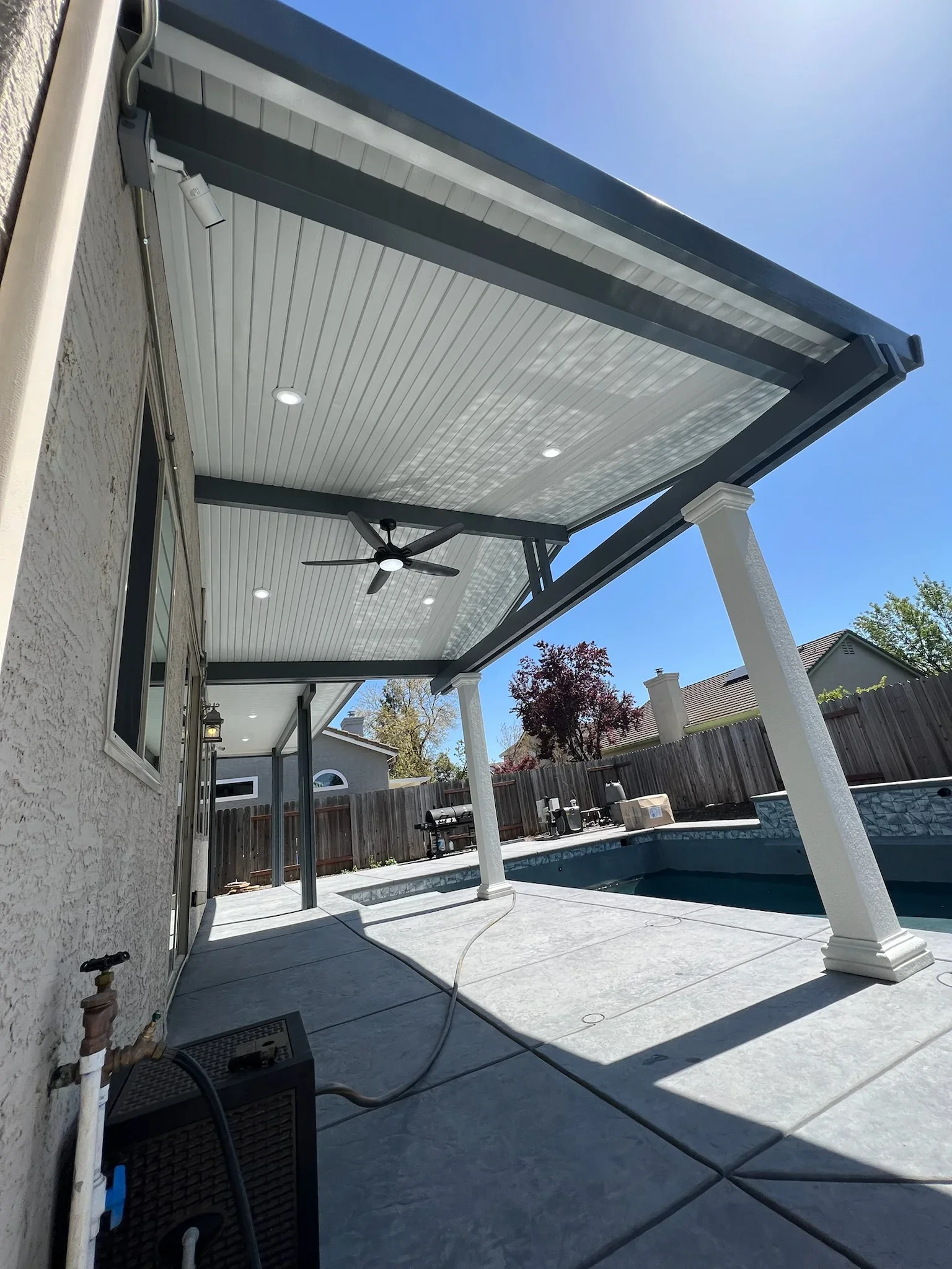 White pergola with polycarbonate roof, LED lights, ceiling fan, and aluminum frame over composite patio deck