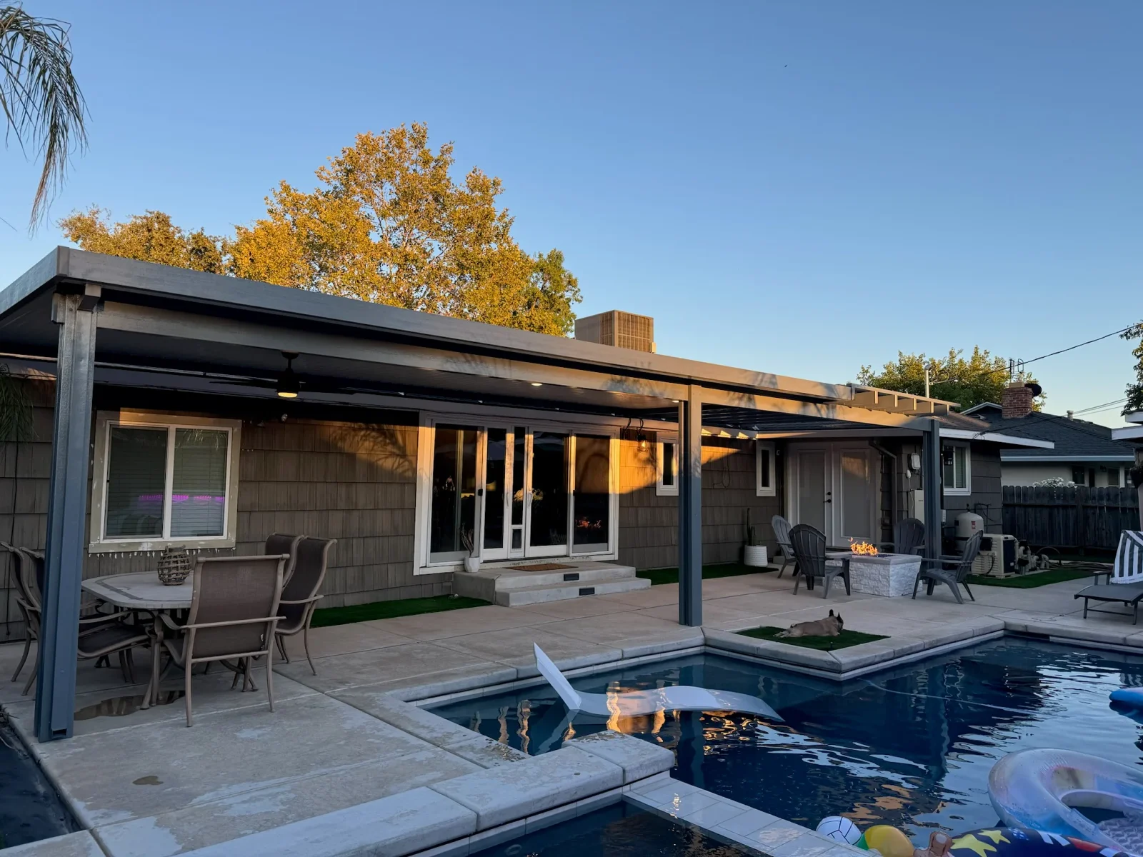 Black aluminum pergola over composite patio with pool, modern home exterior