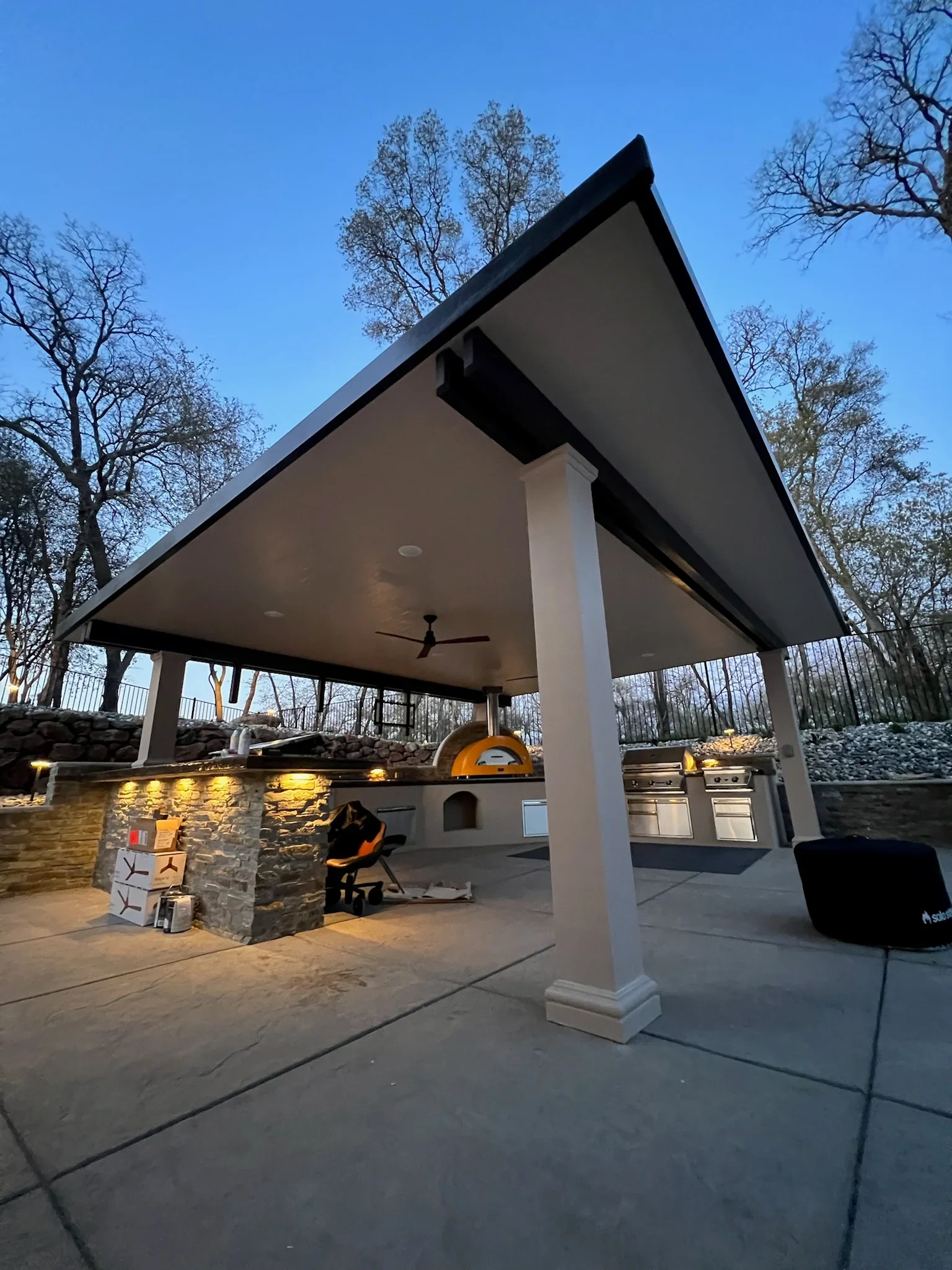 Modern gazebo with gable roof, white column, black trim, stone kitchen base, and yellow pizza oven