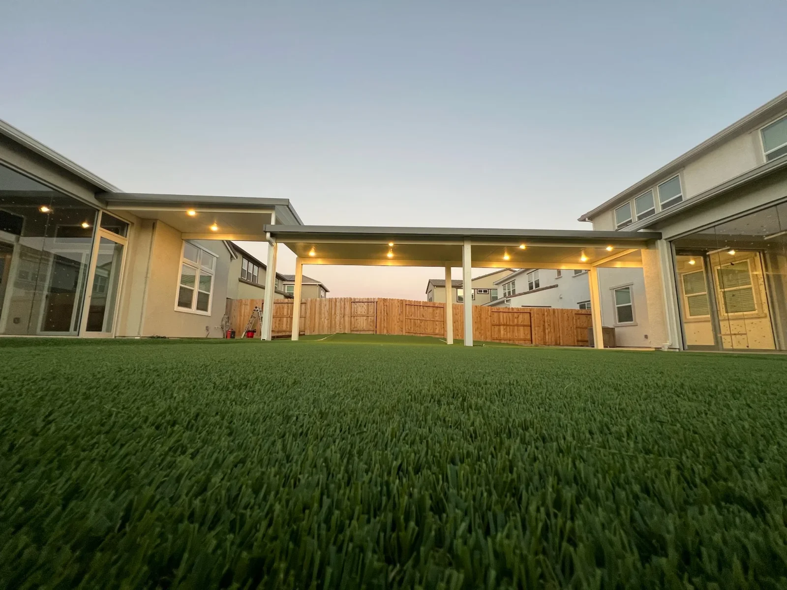 White pergola patio cover with recessed lighting over synthetic turf backyard