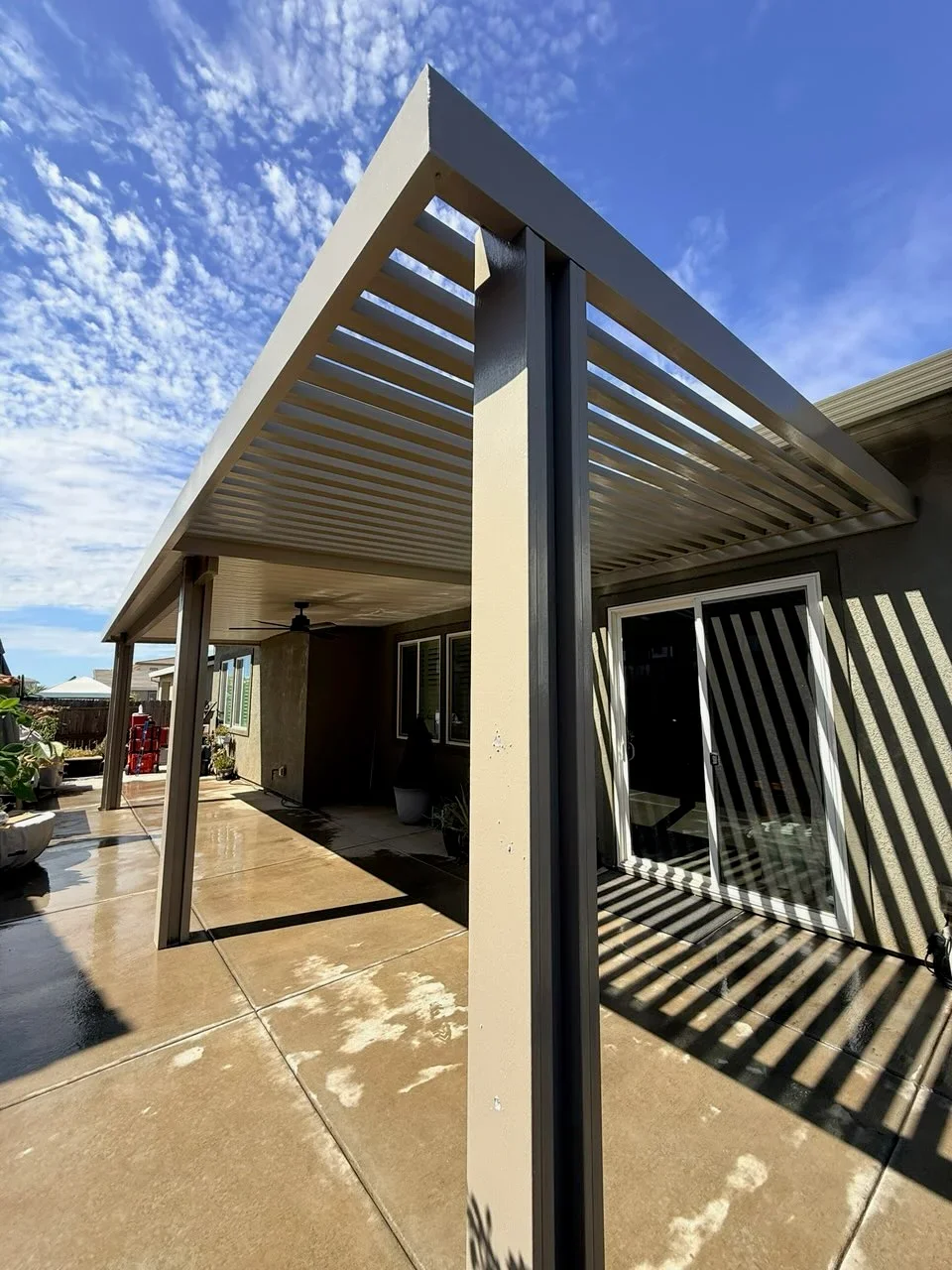 Modern louvered pergola with adjustable aluminum slats over concrete patio, cream posts and dark gray louvers
