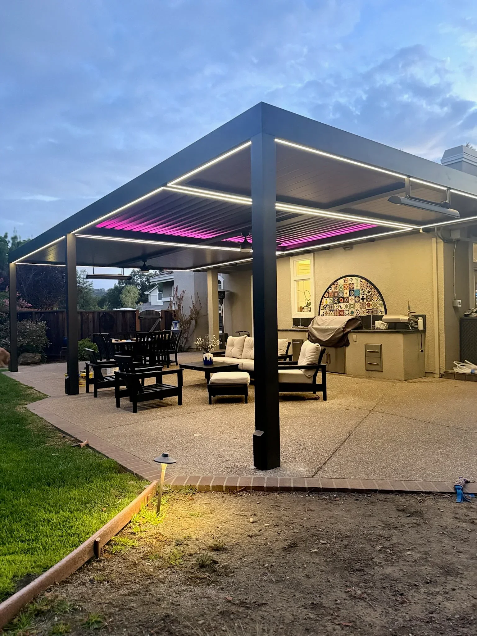 Black aluminum pergola with LED lighting and motorized louver panels over concrete patio