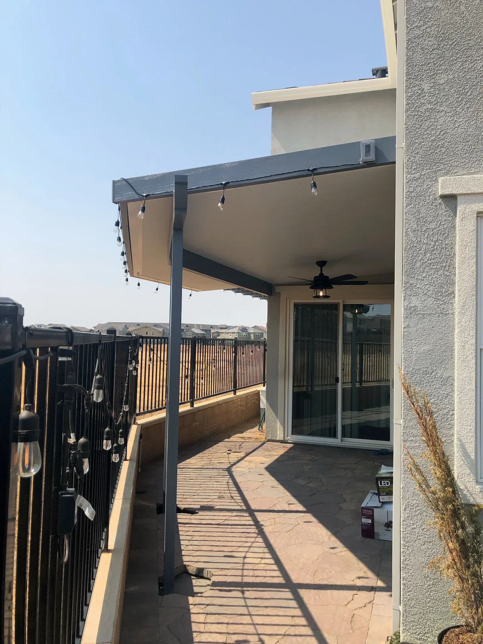 Black steel pergola with retractable tan shade canopy and pendant lighting on residential deck