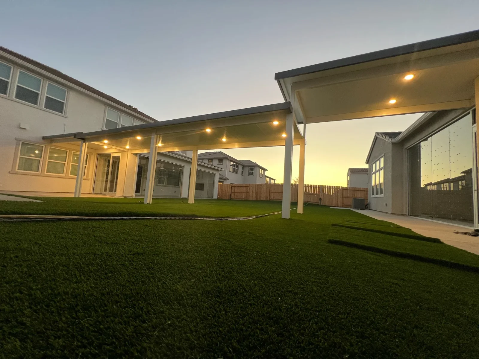 White post pergola with dark beams and recessed lighting over synthetic turf backyard