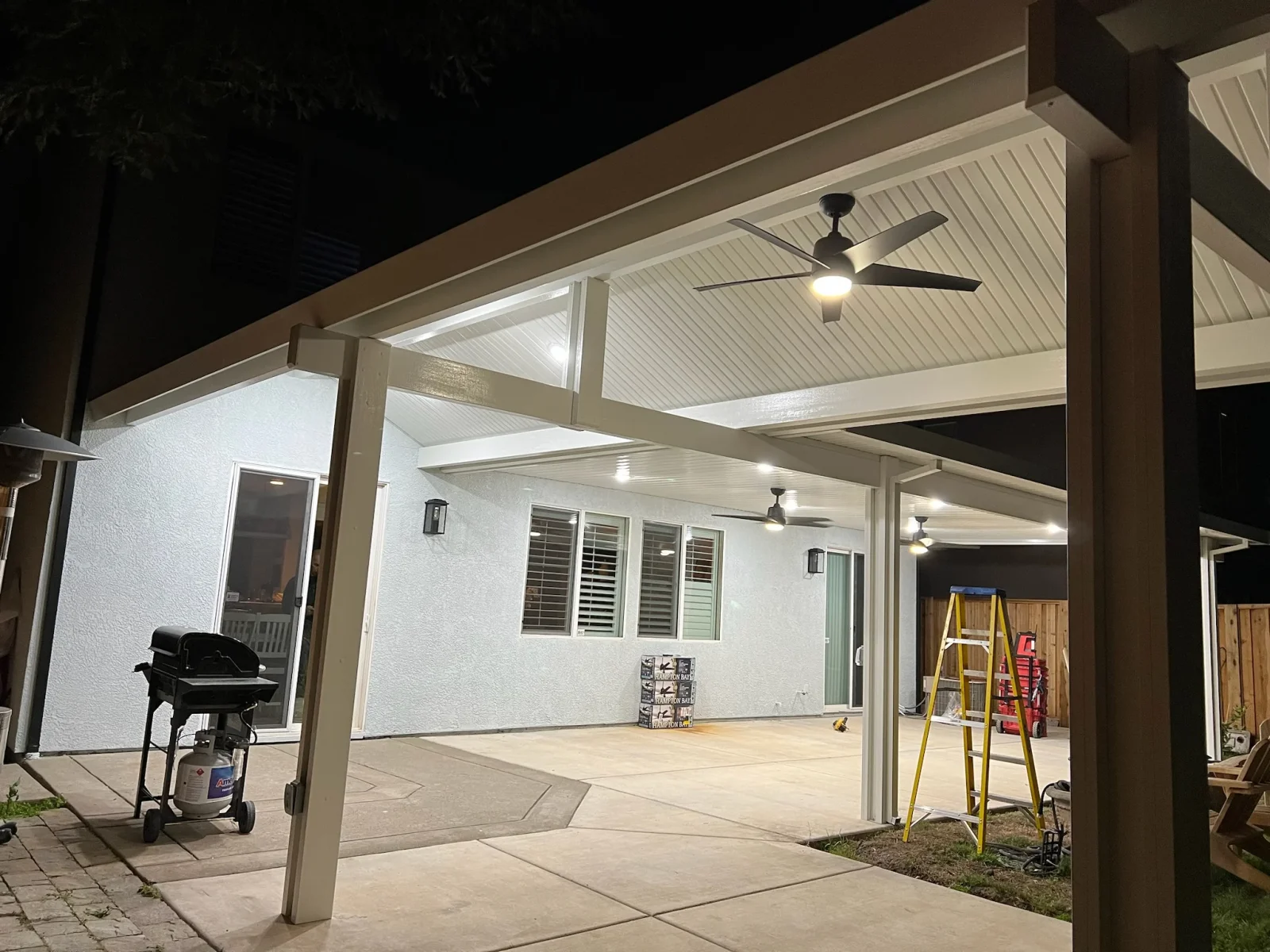 Covered patio with white metal roof, support columns, ceiling fans, and recessed lighting over concrete pad