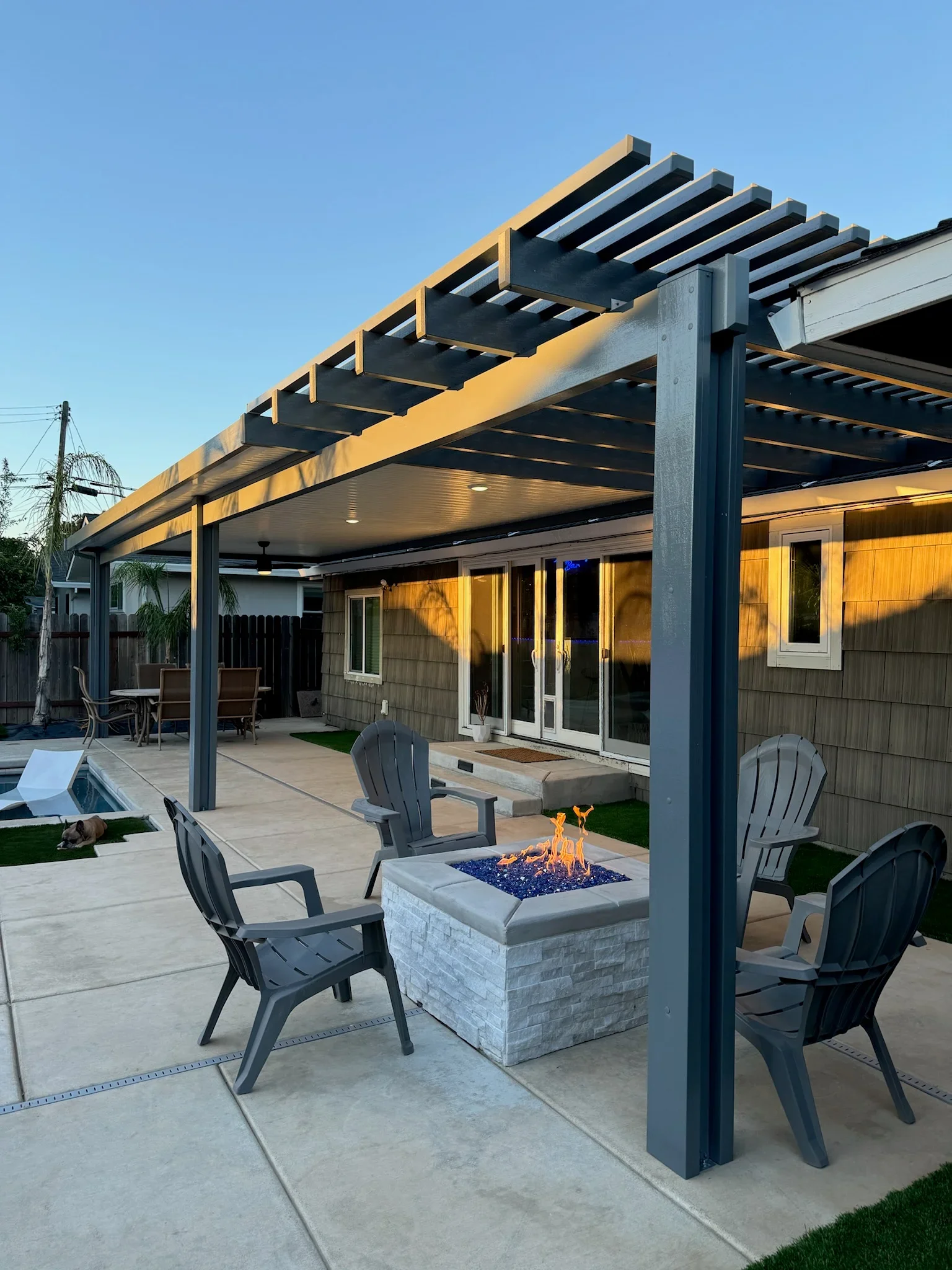 Steel pergola with louvered roof, soffit ceiling, and integrated fire pit on concrete patio