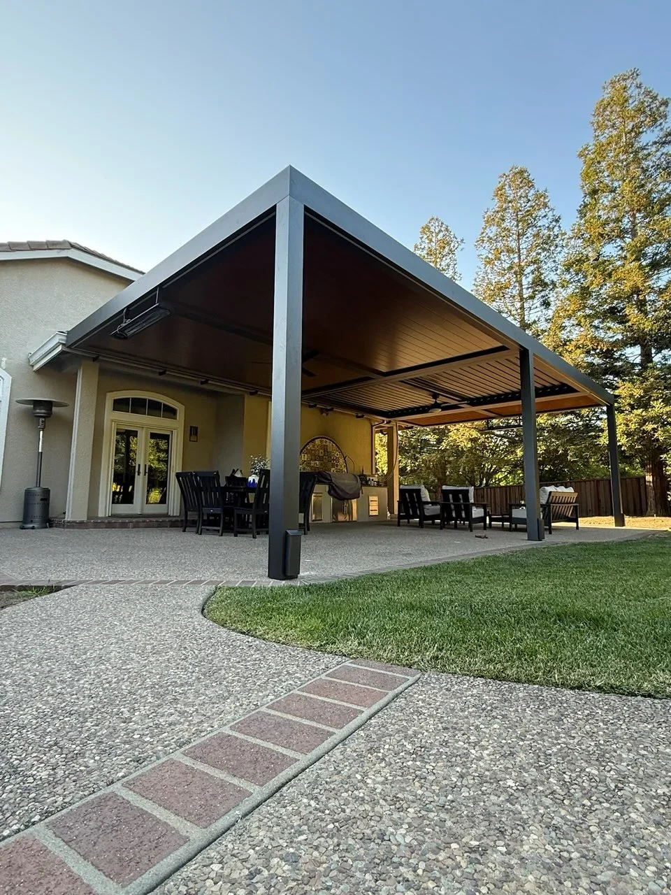 Steel pergola with adjustable louvered roof, black frame, wood ceiling panels, concrete patio