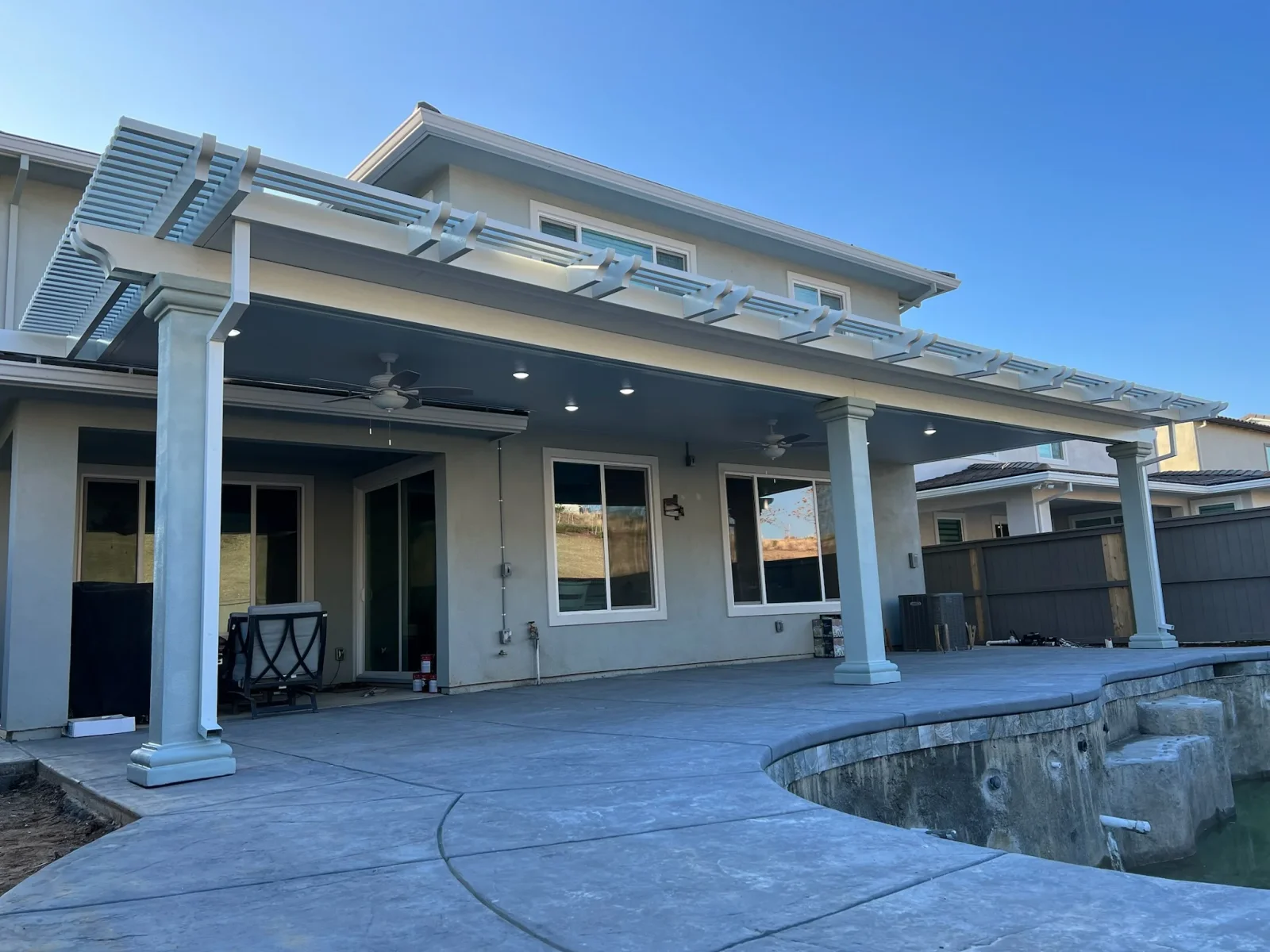 White pergola with louver slats and recessed lighting over stamped concrete patio with support columns