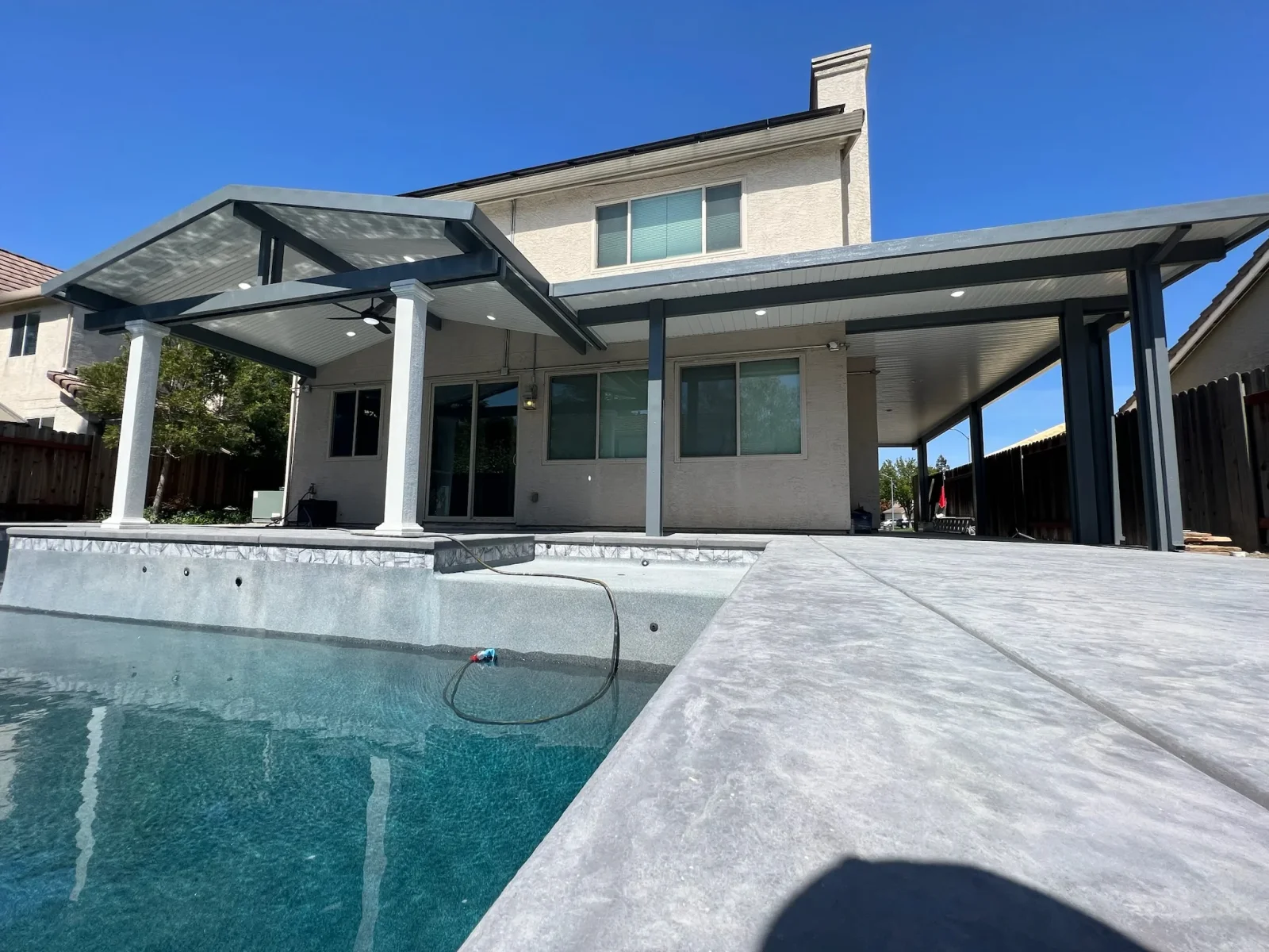 Black aluminum pergola with louvered roof over concrete patio beside residential pool