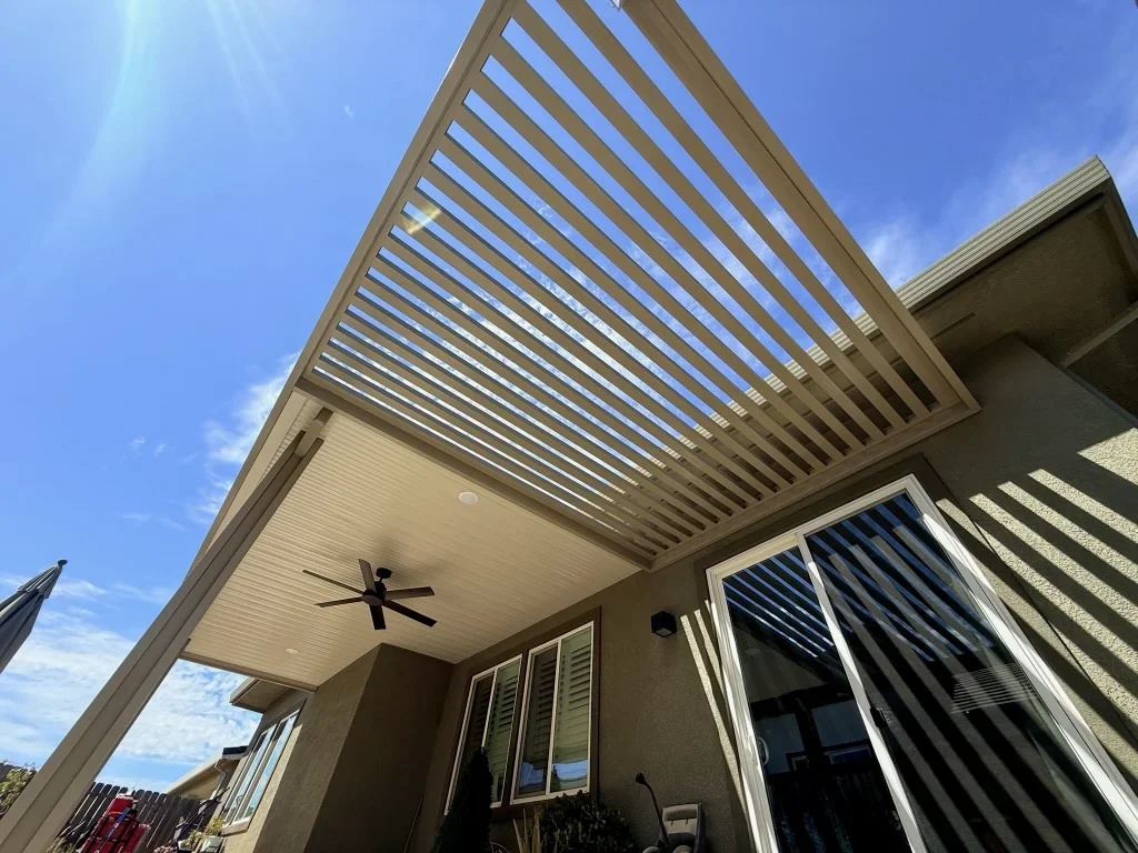 Louvered aluminum pergola with adjustable slats over patio, ceiling fan, and glass doors