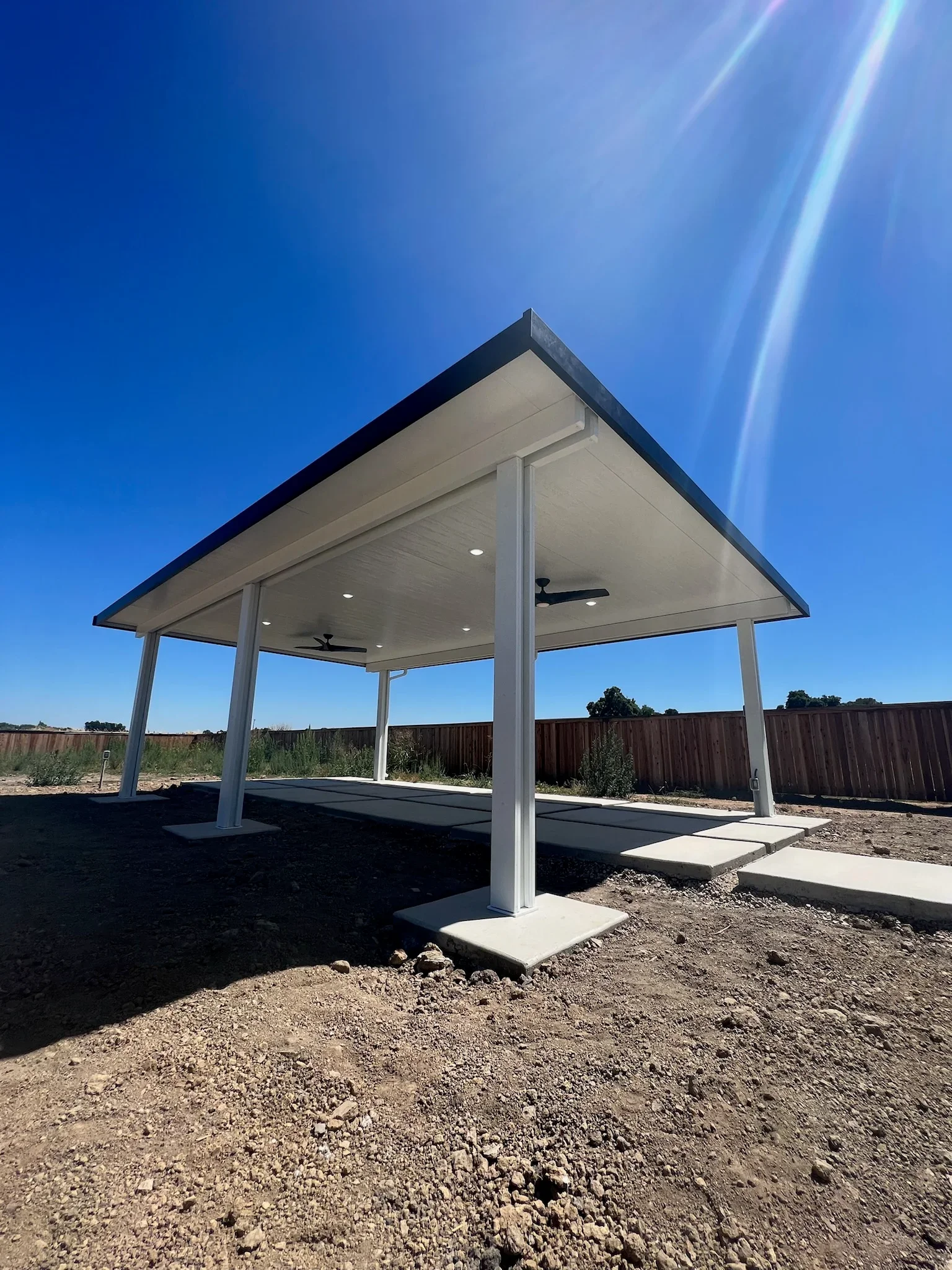 White aluminum gazebo with pitched roof, ceiling fans, and recessed lighting on concrete pads