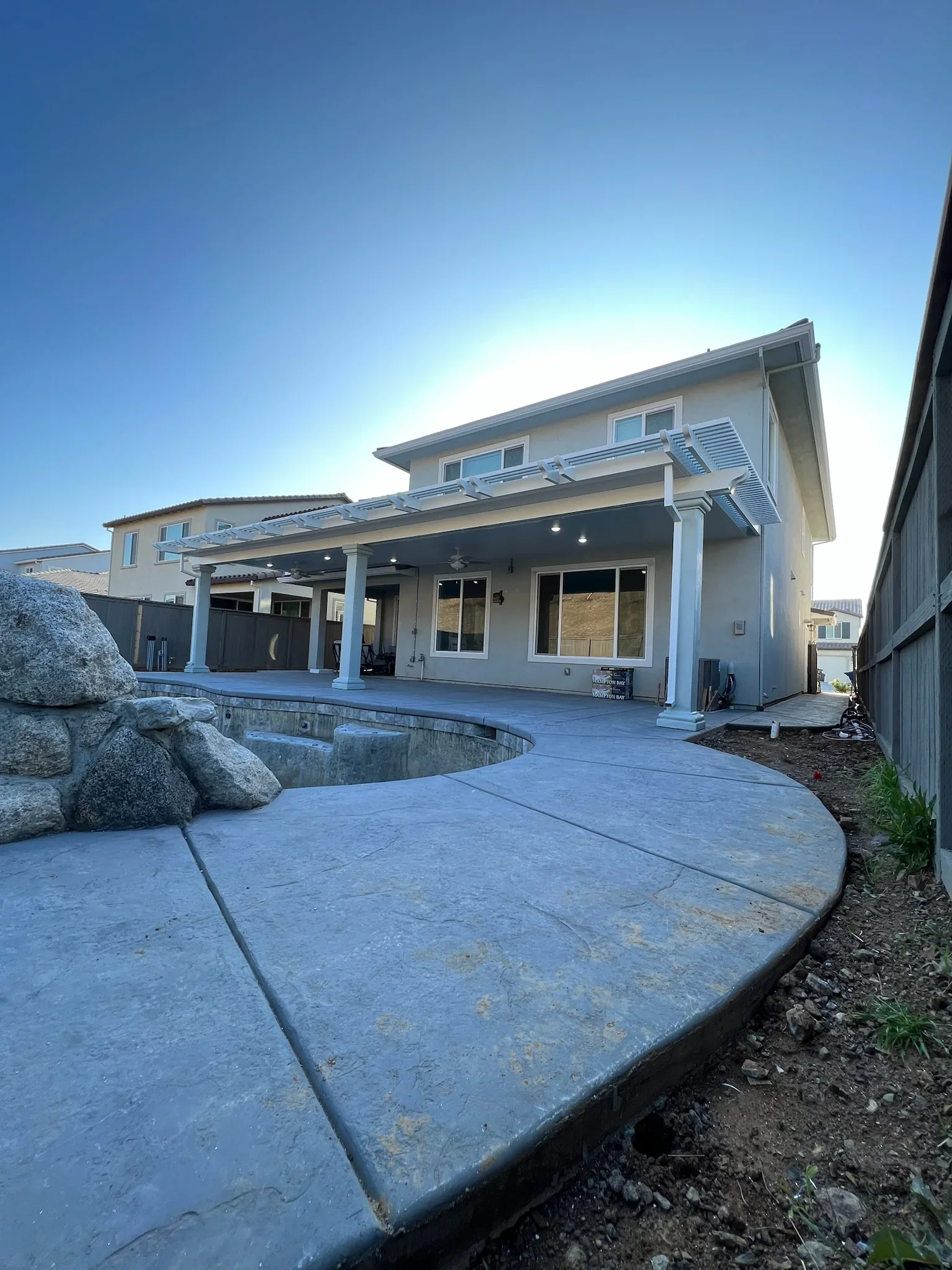 White louvered pergola over concrete patio with boulders and integrated lighting
