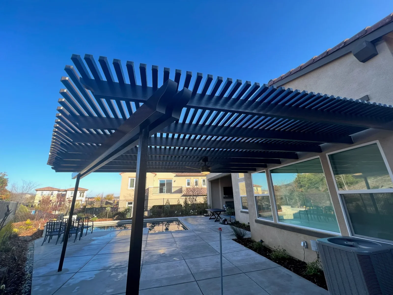 Black aluminum pergola with adjustable louvered roof over concrete patio and pool area