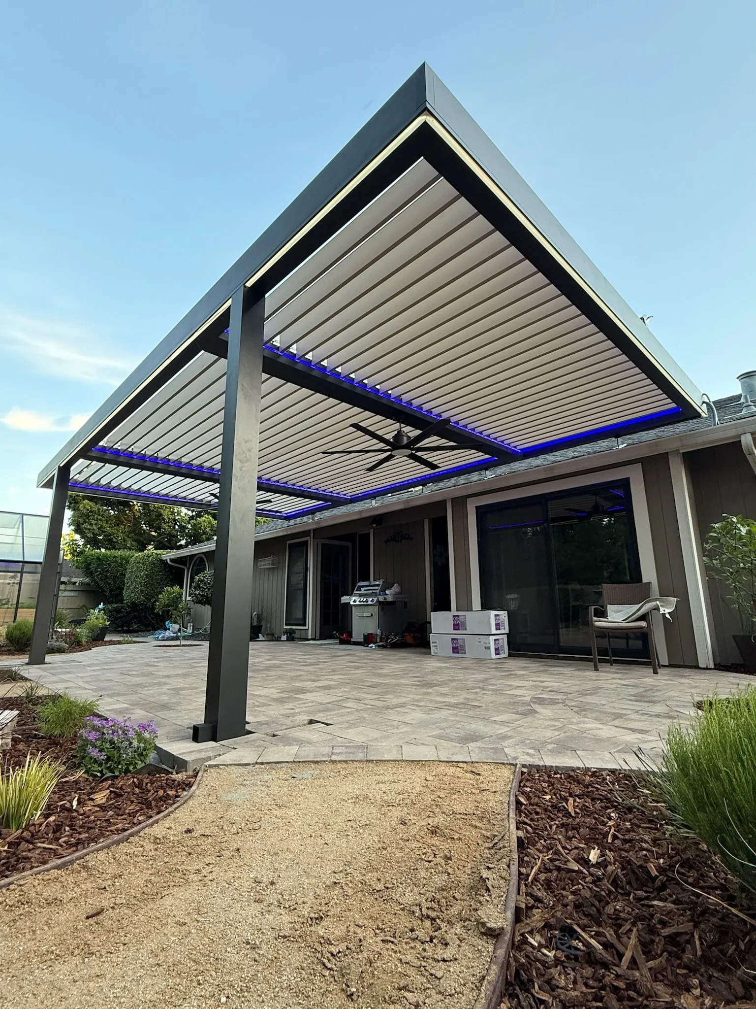 Louvered aluminum pergola with blue LED lighting over patio with stone pavers